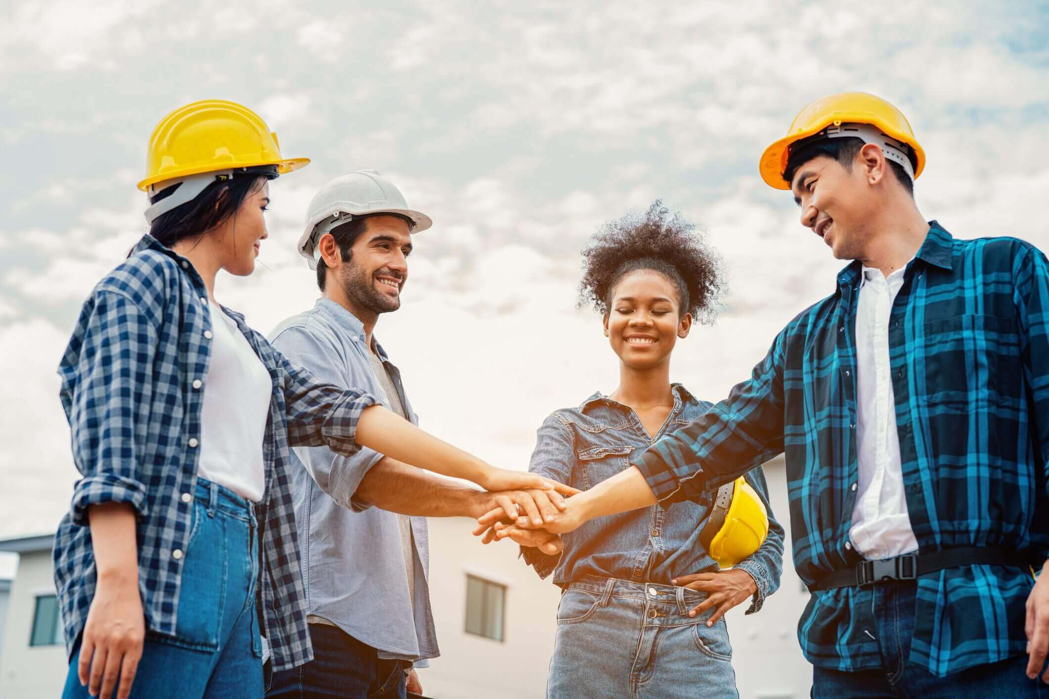 Construction team joining hands outdoors.