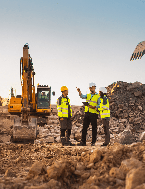 Construction workers discussing site plans near excavator.